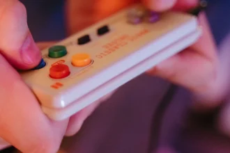 Manette 8BitDo SN30 style SNES tenue en main, boutons d'action colorés, ambiance gaming retro