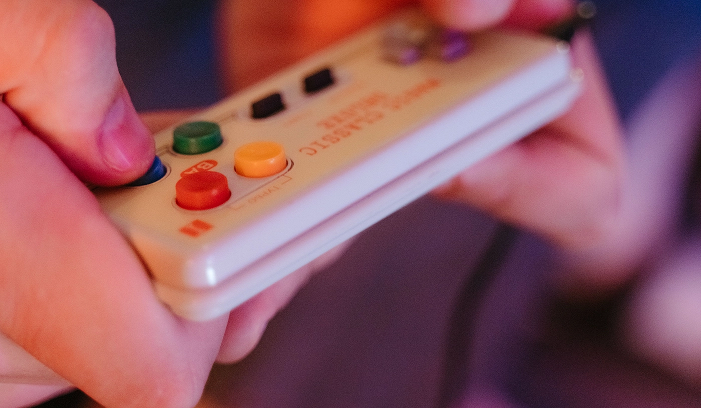 Manette 8BitDo SN30 style SNES tenue en main, boutons d'action colorés, ambiance gaming retro