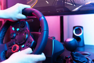 Gros plan sur un joueur qui tient un volant de course sim racing avec pédalier, levier de vitesse et enceinte, ambiance néon bleu et violet